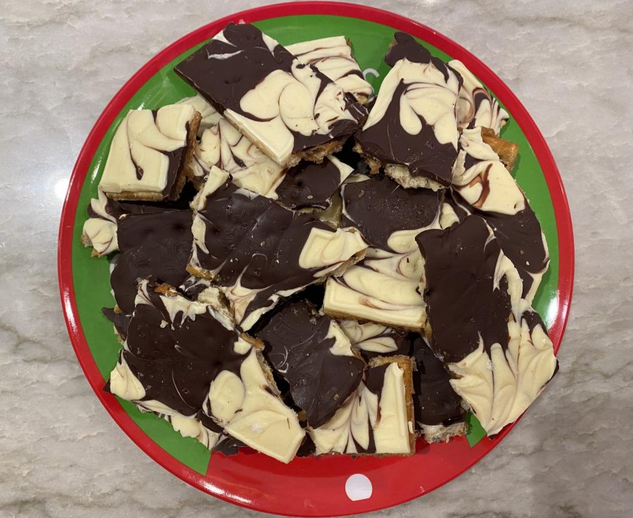 Atop a decorative Christmas-themed plate, freshly made chocolate bark beckons those in need of a sweet treat. The bark combines not only white and dark chocolate, but also salty and sweet flavors with the ingredient of saltine crackers.